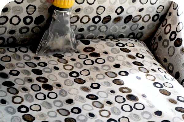 Reinigen van een stoffen meubelstuk met behulp van een professionele tapijtreiniger.